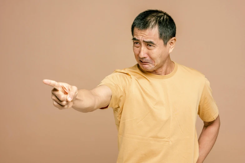 a man in a yellow shirt is pointing at something, trending on pexels, hyperrealism, asian descent, aged 4 0, aggressive pose, brown