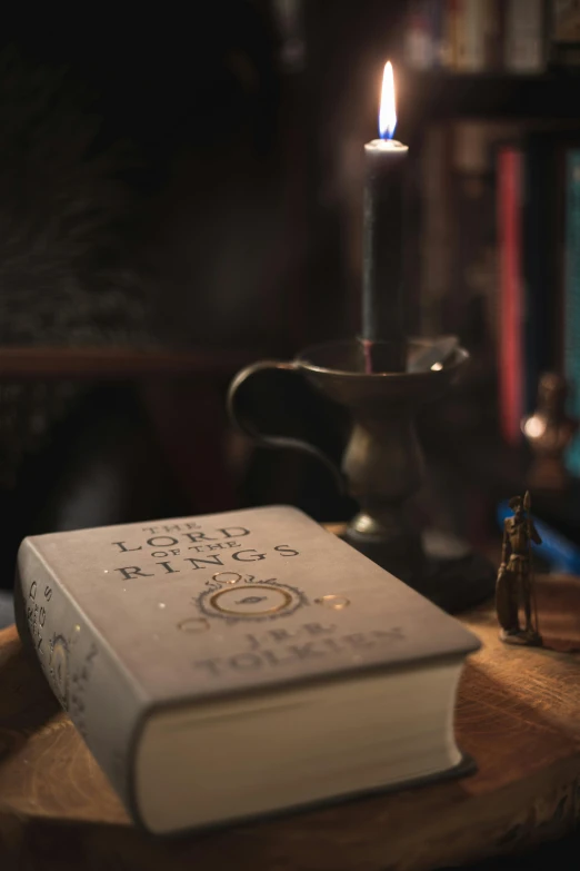 a book sitting on top of a wooden table next to a candle, lord of the rings artifacts, cinematic counter light, 1/60, grey