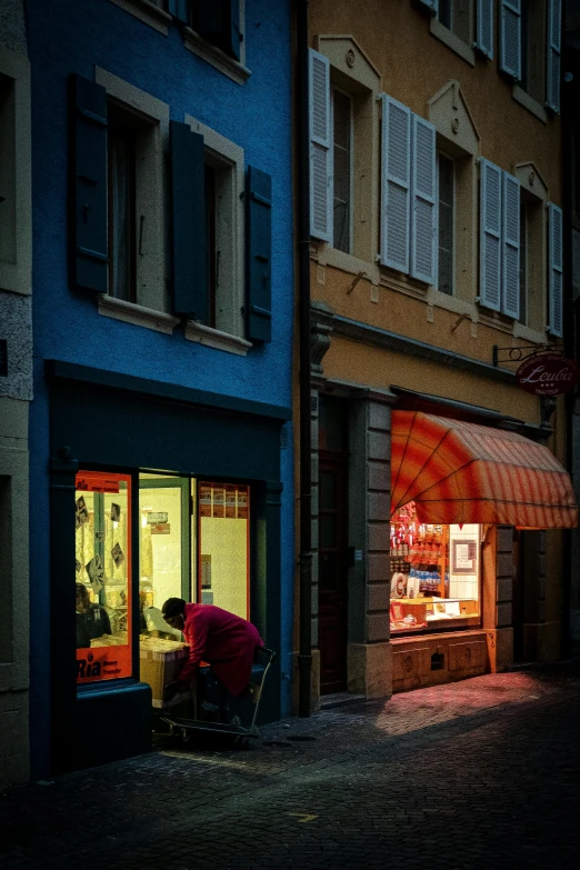 a person sitting at a table in front of a store, by Tobias Stimmer, pexels contest winner, renaissance, reddish exterior lighting, blue shutters on windows, split near the left, prize winning color photo