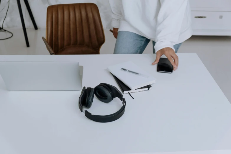 a woman standing in front of a desk with a laptop and headphones, by Andries Stock, trending on pexels, miscellaneous objects, man sitting facing away, black on white, items and gadget