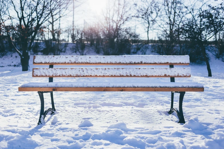 a wooden bench covered in snow in a park, unsplash, in the sun, background image, no repeat, some people are sitting