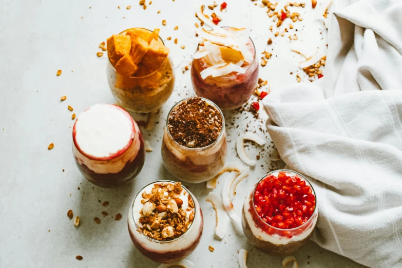 a number of desserts in jars on a table, a portrait, by Emma Andijewska, trending on pexels, tropical, the god of oatmeal, bowl, studio shot