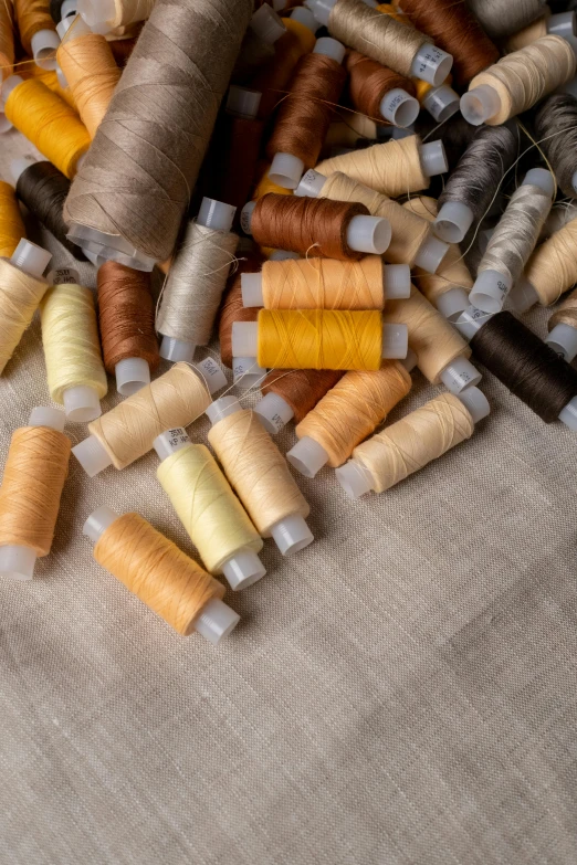 a pile of spools of thread sitting on top of a table, a cross stitch, by Alison Geissler, trending on unsplash, renaissance, muted brown yellow and blacks, made of fabric, thumbnail, silk colors