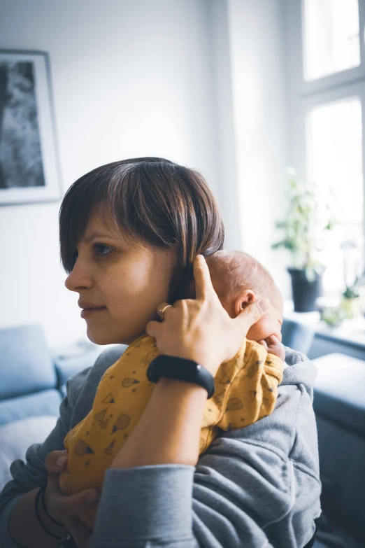 a woman holding a baby in her arms, by Sebastian Spreng, unsplash, with head phones, at home, sideburns, right hand side profile