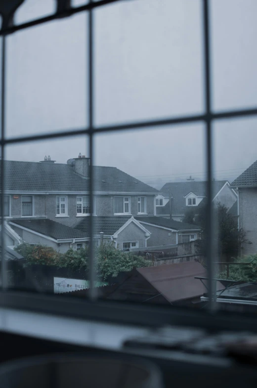 a view of a neighborhood through a window, a picture, unsplash, realism, under a gray foggy sky, 8 k film still, roofs, rainy evening