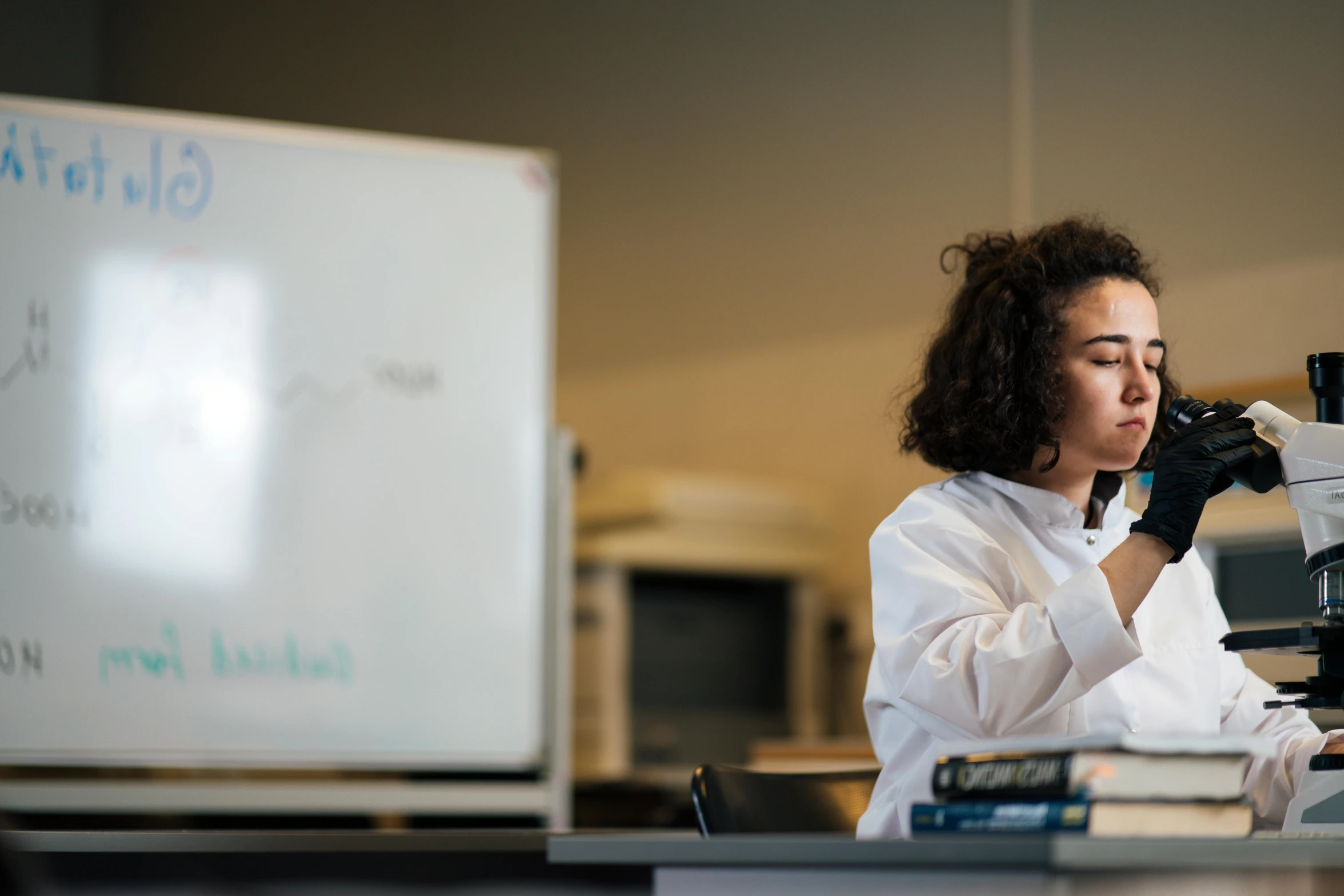 a woman in a lab coat looking through a microscope, unsplash, ashcan school, whiteboards, riyahd cassiem, lit from the side, te pae