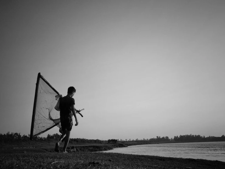 a black and white photo of a man holding a kite, by Sunil Das, pexels, fishing, assamese, man is carrying a rifle, netting