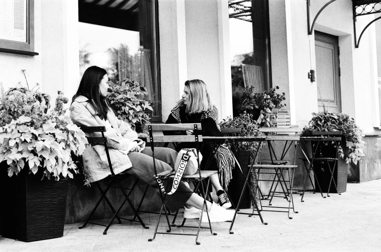 a woman sitting at a table talking on a cell phone, a black and white photo, inspired by Ruth Orkin, realism, two girls, 🌸 🌼 💮, 35mm!!! 1990, cafe