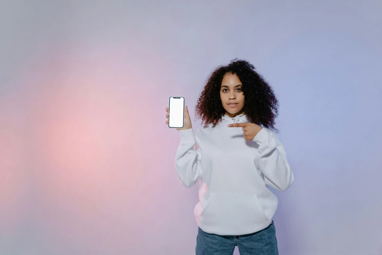 a woman in a white hoodie holding a cell phone, a photo, trending on pexels, power pose, curly haired, ( ( brown skin ) ), with index finger