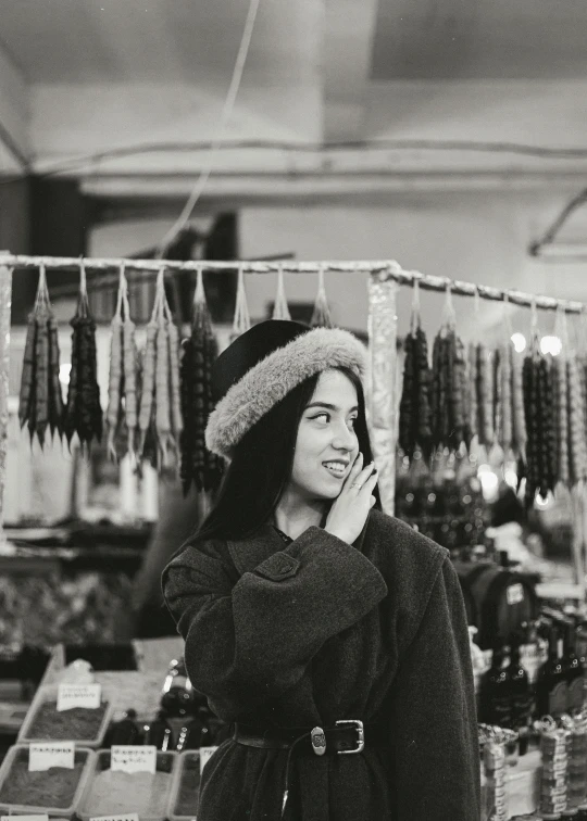 a black and white photo of a woman talking on a cell phone, a black and white photo, by Lucia Peka, trending on pexels, market stalls, black haired girl wearing hoodie, wearing wool hat, ukrainian