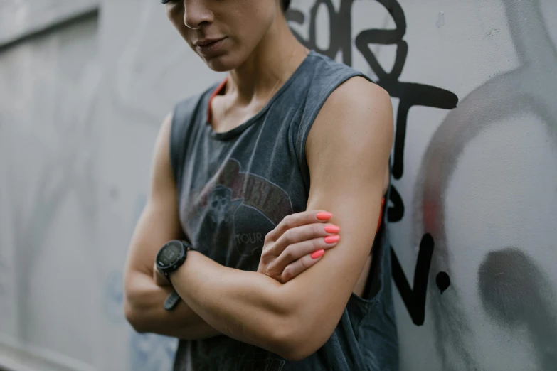 a woman leaning against a wall with her arms crossed, a tattoo, trending on pexels, graffiti, wearing a muscle tee shirt, painted nails, androgynous person, detaild