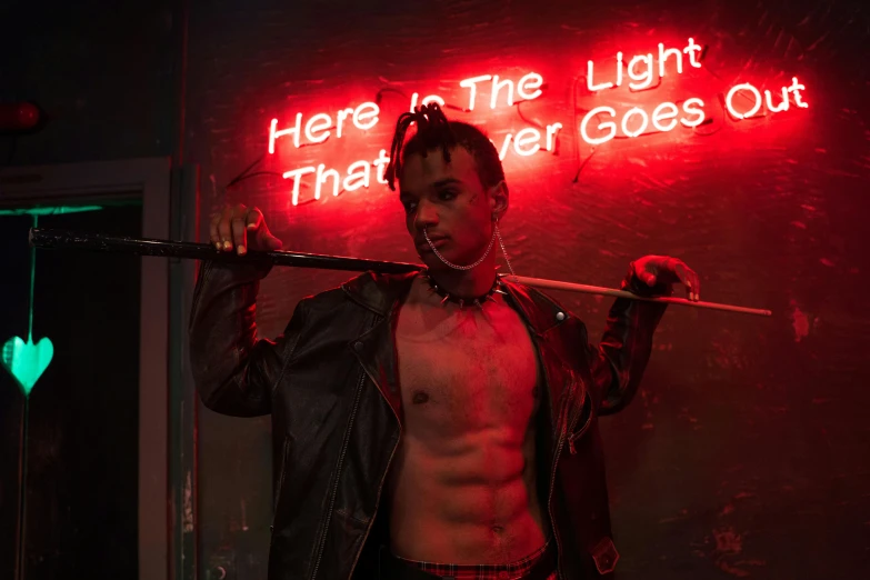 a man standing in front of a neon sign that says here is the light that never goes out, an album cover, inspired by Nan Goldin, pexels contest winner, in a leather corset, xxxtentacion, action scene from the film, [ theatrical ]