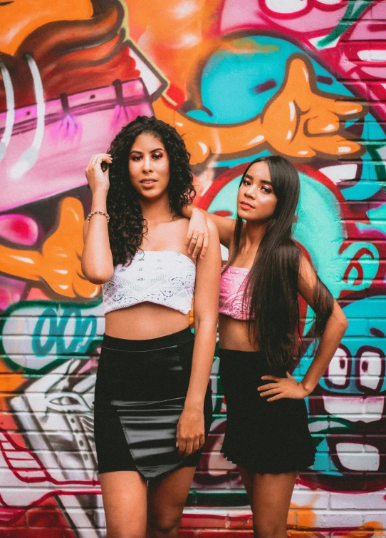 two women standing in front of a graffiti wall, an album cover, trending on pexels, wearing crop top, latinas, headshot profile picture, teenagers