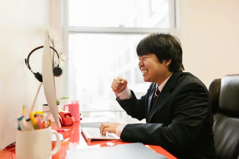 a man sitting at a desk in front of a computer, inspired by Miyamoto, pexels contest winner, wearing a black and red suit, giggling, hong june hyung, professional profile picture