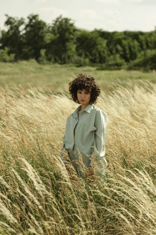 a woman standing in a field of tall grass, an album cover, curly and short top hair, wearing hay coat, thoughtful pose, summertime