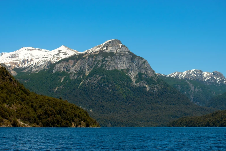 a large body of water with a mountain in the background, patagonian, lush surroundings, exterior photo, clear blue skies