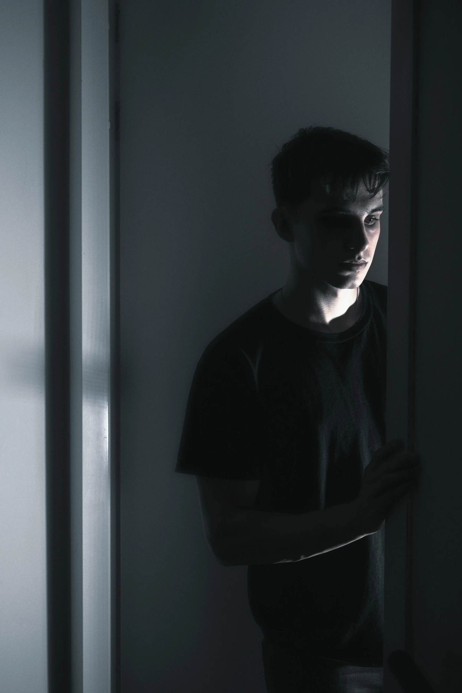 a man standing in a dark room in front of a window, an album cover, inspired by Jean Malouel, pexels contest winner, leaning on door, backlit face, male teenager, spying