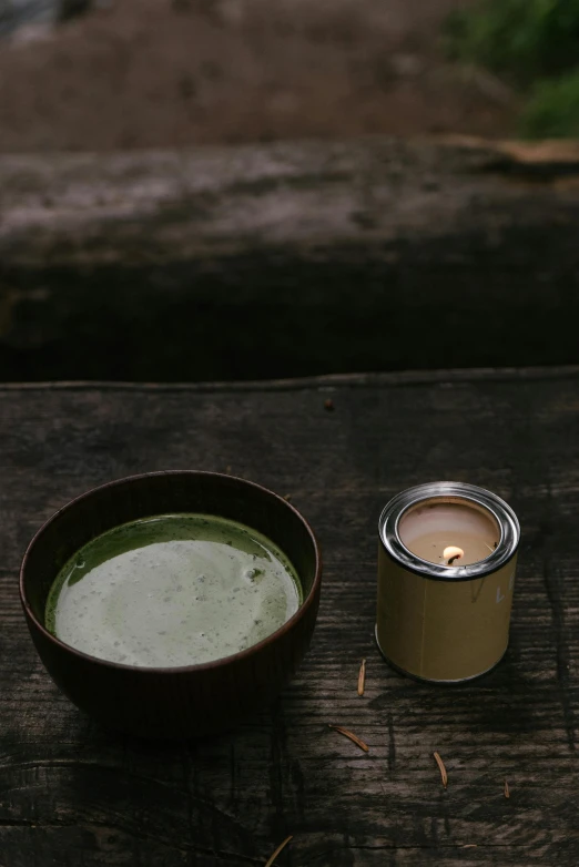 a bowl of soup next to a candle on a wooden table, inspired by Kanō Shōsenin, hurufiyya, forest picnic, mate, dark green water, soymilk