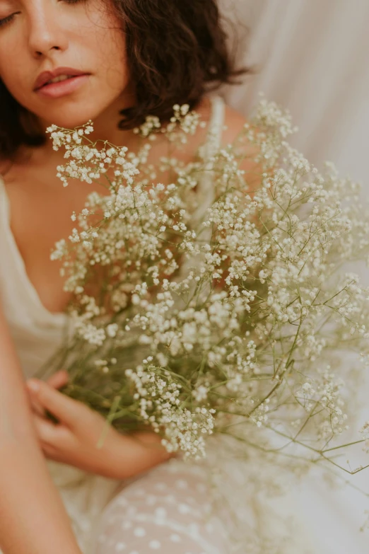 a woman sitting on a bed holding a bouquet of flowers, inspired by Elsa Bleda, gypsophila, zoomed in, ethereal skin, medium details