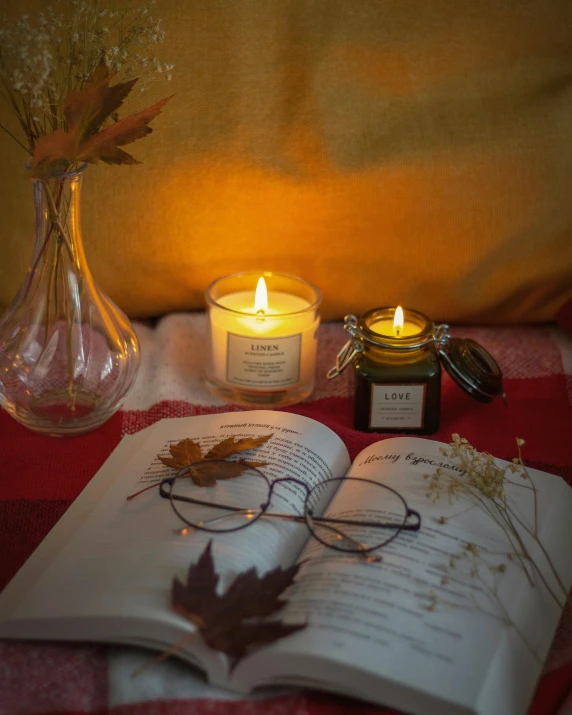 an open book sitting on top of a table next to a candle, a still life, inspired by Louis Hersent, unsplash contest winner, square glasses, autumnal colours, product display photograph, angled shot