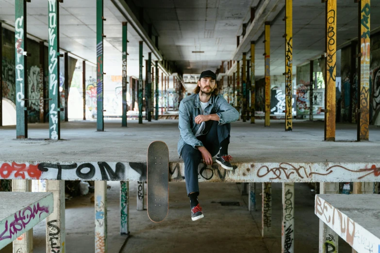 a man sitting on a bench with a skateboard, a portrait, pexels contest winner, graffiti, in an abandoned mall, aboriginal australian hipster, sitting under bridge, promotional image