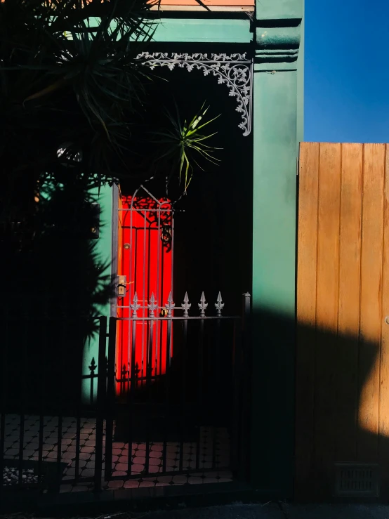 a red fire hydrant sitting in front of a green building, by Andrew Allan, unsplash contest winner, australian tonalism, standing astride a gate, late afternoon sun, magic doorway, multicoloured