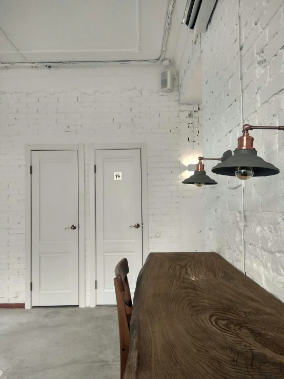 a long wooden table sitting in front of a white brick wall, door to lab, comfy lighting, listing image, white ceiling