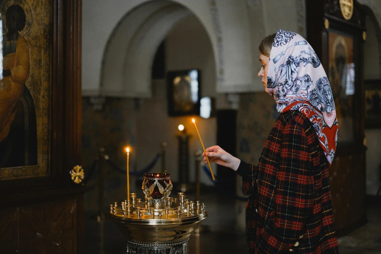 a woman lighting a candle in a church, by Julia Pishtar, pexels, hurufiyya, russian clothes, wearing a grey robe, brown, swedish