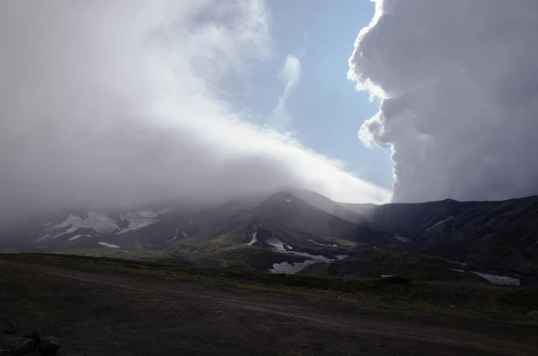 a large plume of smoke coming out of a mountain, by Muggur, pexels contest winner, hurufiyya, storm clouds in the distance, lariennechan, puffy white clouds, view from ground