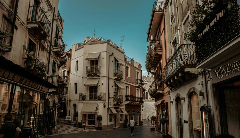 a couple of people walking down a street next to tall buildings, a photo, pexels contest winner, neoclassicism, taormina amphitheatre, house's and shops and buildings, blonde, square