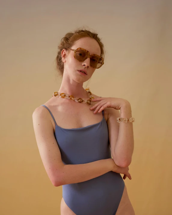 a woman in a blue bodysuit and sunglasses, inspired by Elsa Bleda, renaissance, puka shell necklace, muted brown, curated collection, translucent