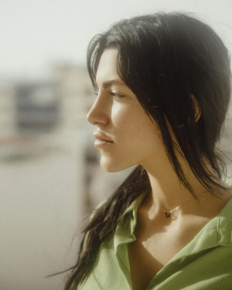a woman in a green shirt looking out a window, trending on pexels, hyperrealism, female with long black hair, queer woman, focused on her neck, young middle eastern woman
