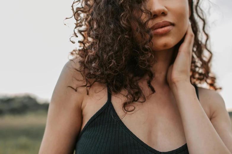 a woman with curly hair standing in a field, trending on pexels, decolletage, with textured hair and skin, wearing a camisole, neck zoomed in