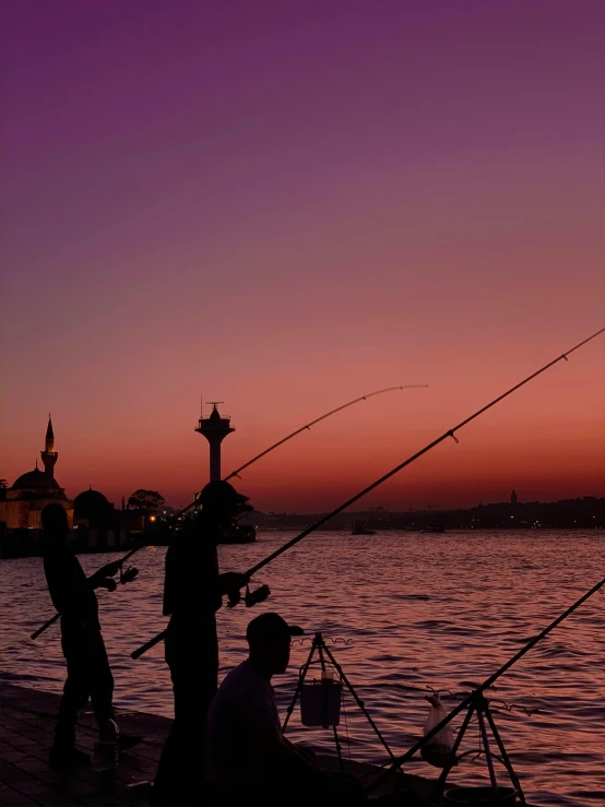 a group of people standing on top of a pier next to a body of water, fishing, during the night, istanbul, pink golden hour