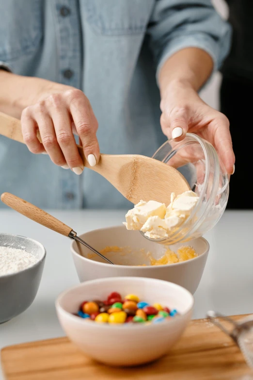 a woman mixing ingredients in a bowl with a wooden spoon, cheesy, cupcake, promo photo, tabletop