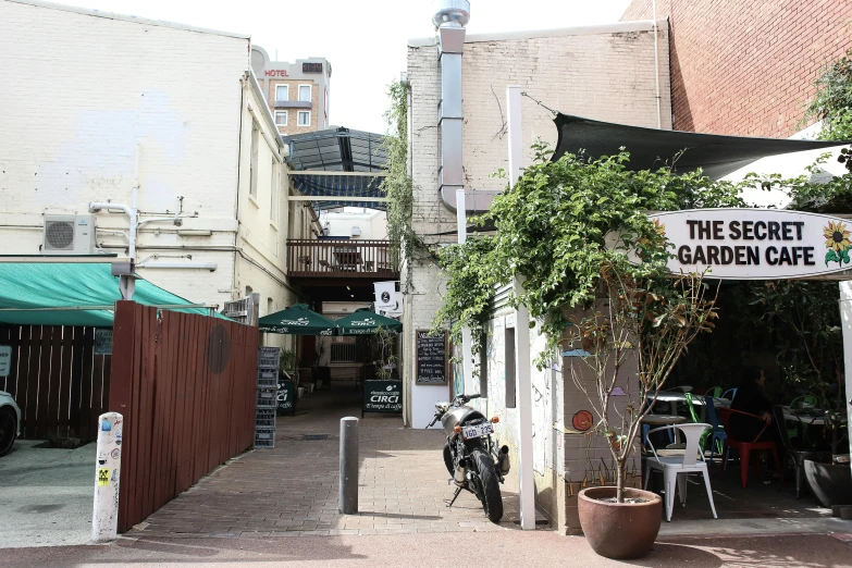 a building with a sign that says the secret garden cafe, a photo, unsplash, temporary art, shady alleys, manly, alexandria\'s genesis, a middle-shot from front