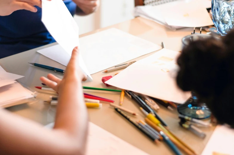 a couple of people that are sitting at a table, a child's drawing, pexels contest winner, holding pencil, 9 9 designs, thumbnail, mid shot photo