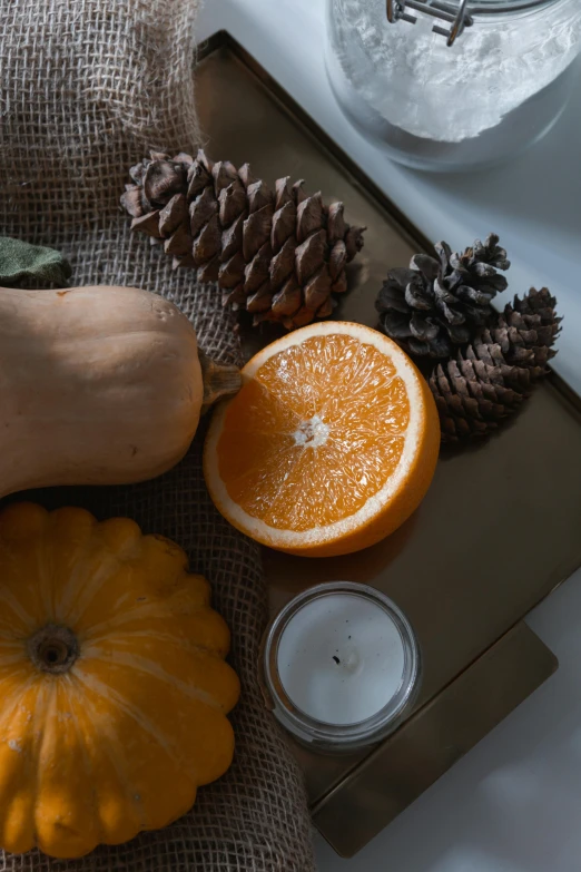 a table topped with pumpkins, oranges and pine cones, on a gray background, sitting on a mocha-colored table, - 9, low quality photo