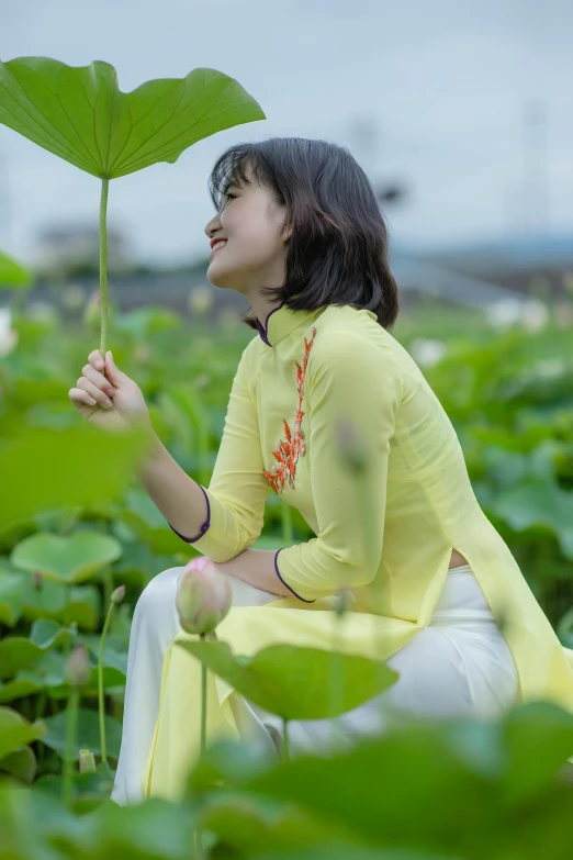a woman sitting on top of a lush green field, inspired by Cui Bai, happening, ao dai, chilling on a leaf, yellow, profile image