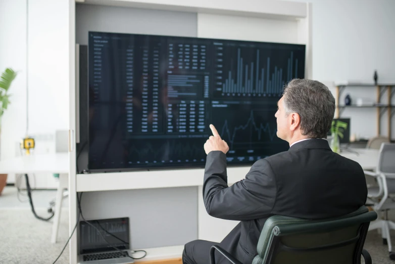 a man sitting in a chair pointing at a computer screen, graphs, 15081959 21121991 01012000 4k, high-quality photo, liam brazier