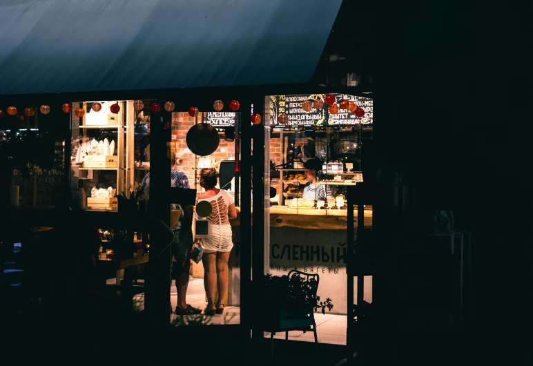 a couple of people standing outside of a store, by Lee Loughridge, pexels contest winner, cafe lighting, bakery, summer night, thumbnail