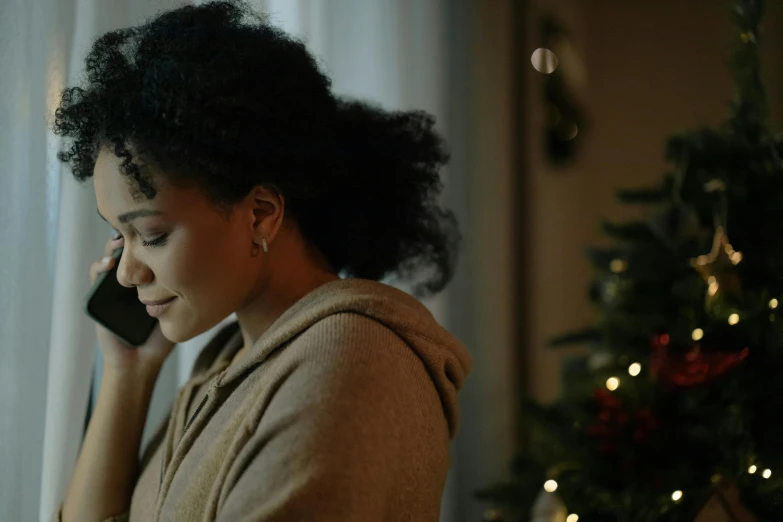 a woman talking on a cell phone in front of a christmas tree, a photo, pexels, black young woman, sorrow, moviestill, arm around her neck