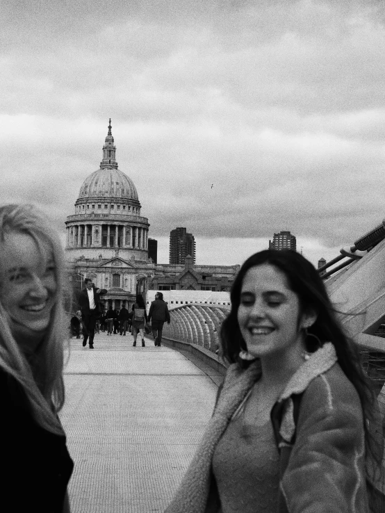 two women standing next to each other on a bridge, a black and white photo, inspired by Thomas Struth, happening, the fabulous city of london, smile like a sphinx, cathedral!!!!!, grainy movie still