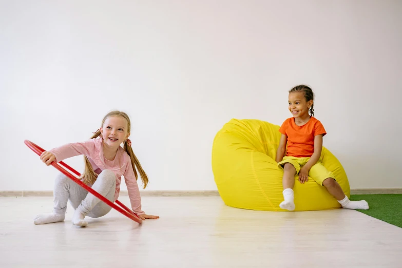 two children sitting on bean bags in a room, pexels contest winner, yellow and red, activity play centre, circular, two girls