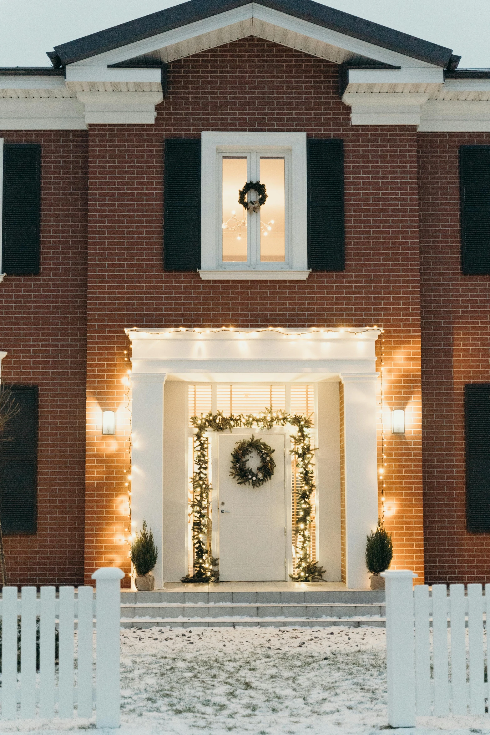 a white picketer in front of a red brick house, a digital rendering, pexels contest winner, christmas lights, symmetrical doorway, architectural digest photo, colonial style