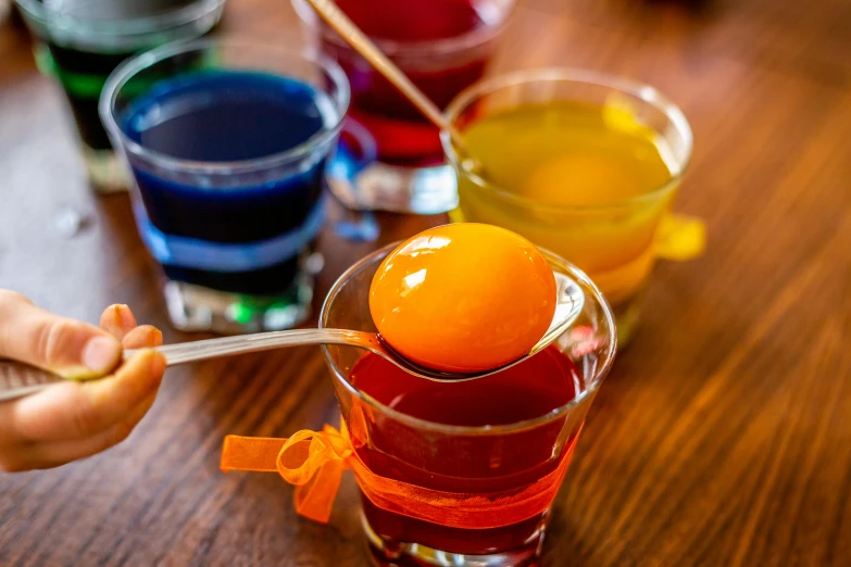 a close up of a person holding a spoon with an orange on it, beakers of colored liquid, holding easter eggs, ots shot, epicurious