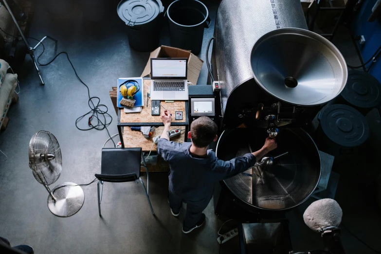 a man sitting at a table working on a laptop, by Matthias Stom, pexels contest winner, arbeitsrat für kunst, coffee machine, aerial view from above, boiler room, aussie baristas