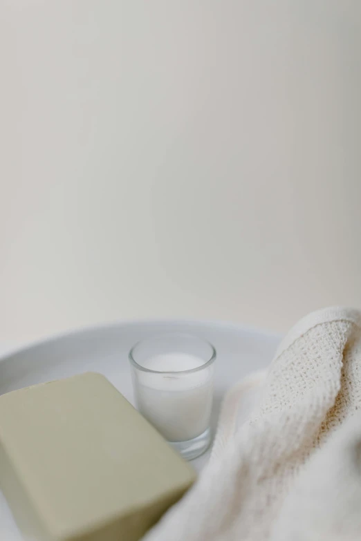 a white plate topped with a piece of butter next to a glass of milk, unsplash, minimalism, towels, soap, silver，ivory, candle