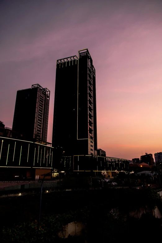 a couple of tall buildings next to a body of water, an album cover, south jakarta, neon backlit, sundown, low quality photo