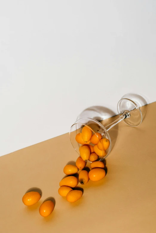 a glass filled with oranges sitting on top of a table, by Nina Hamnett, trending on unsplash, photorealism, holding maracas, silver and yellow color scheme, beans, minimalist composition